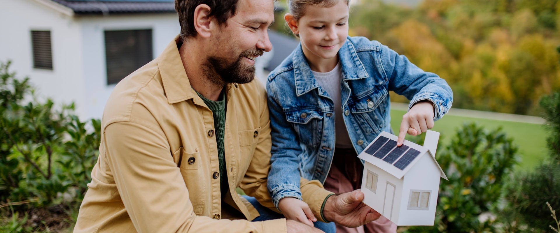 Little girl with her dad holding paper model of house with solar panels, explaining how it works.Alternative energy, saving resources and sustainable lifestyle concept.