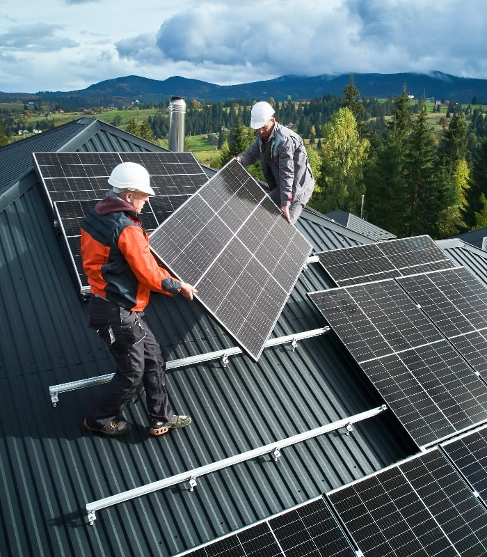 Workers building solar panel system on roof of house. Men technicians in helmets carrying photovoltaic solar module outdoors. Concept of alternative and renewable energy.