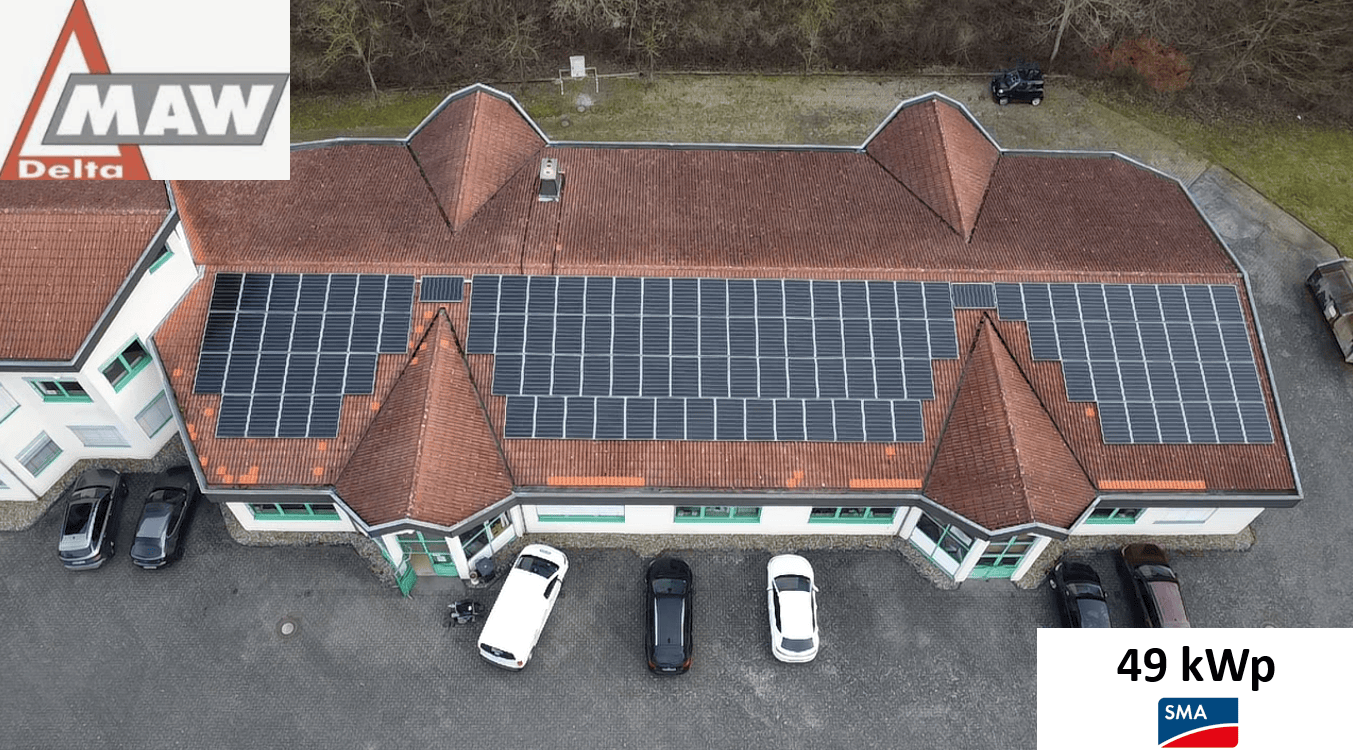 Ziegelhaus mit Solarpanels und parkenden Autos; Dachziegel rot, Solarpanels dunkel.