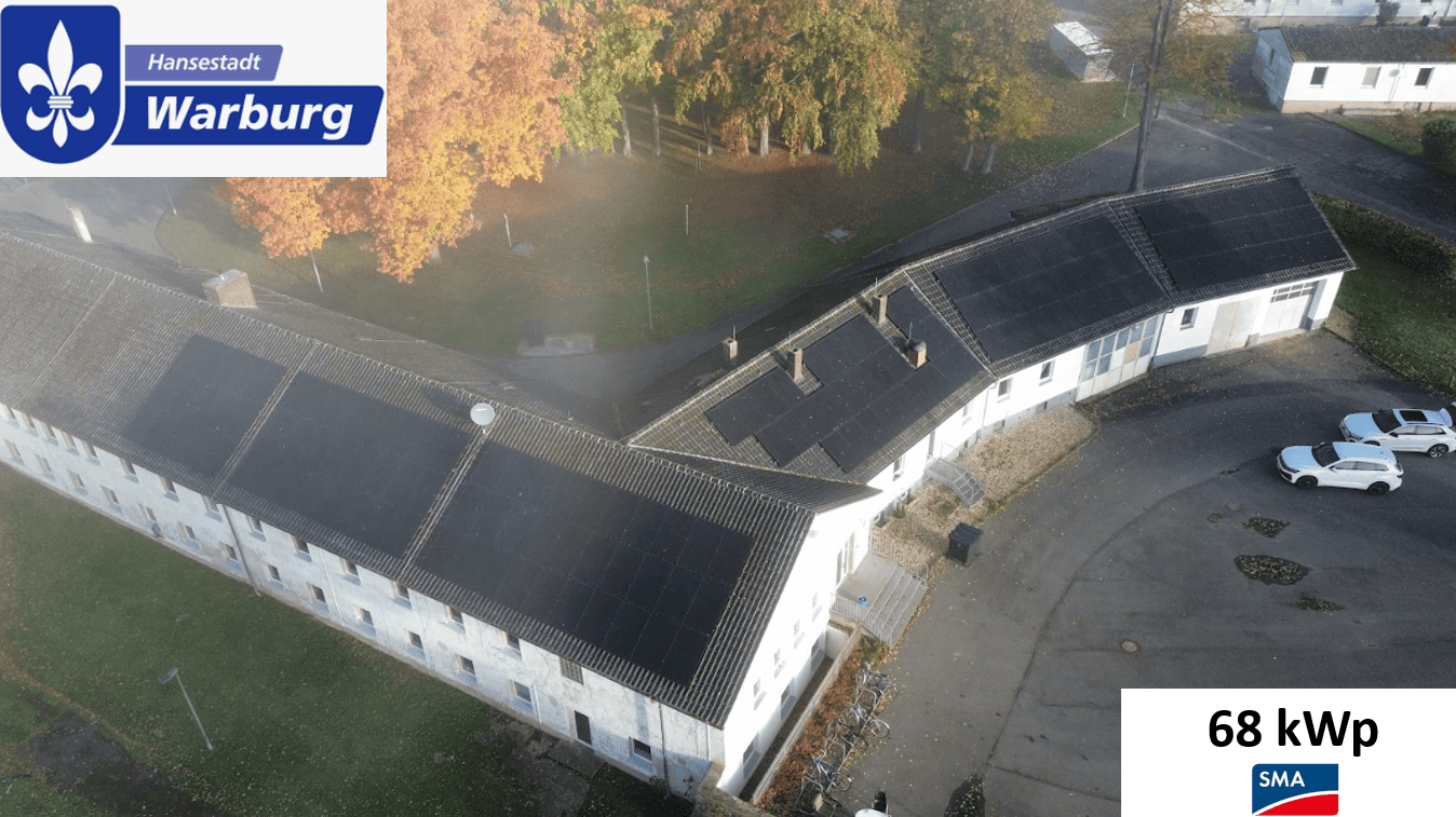 Luftaufnahme eines Gebäudes mit Solaranlagen auf dem Dach und buntem Herbstlaub im Hintergrund.